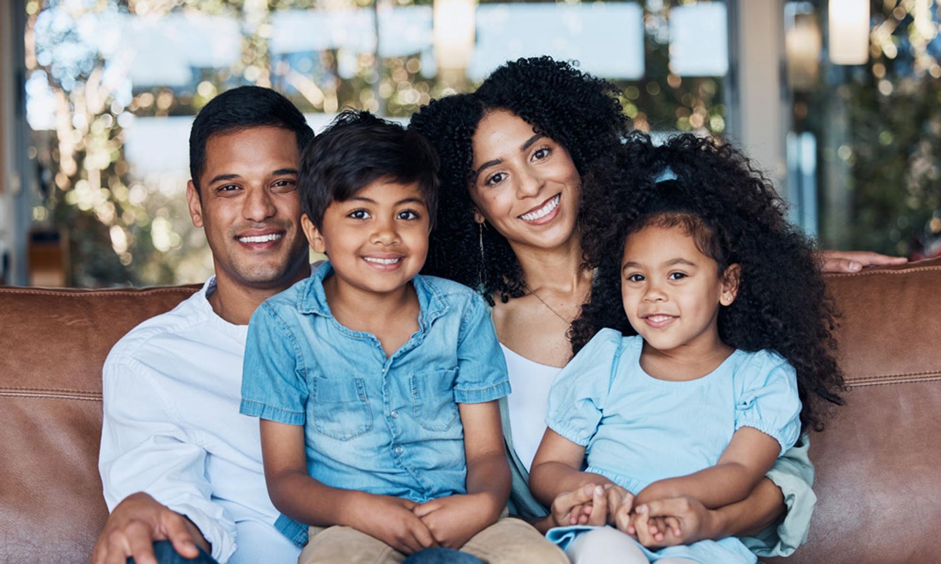 A family of four sitting together on a leather couch, all smiling and looking toward the camera.