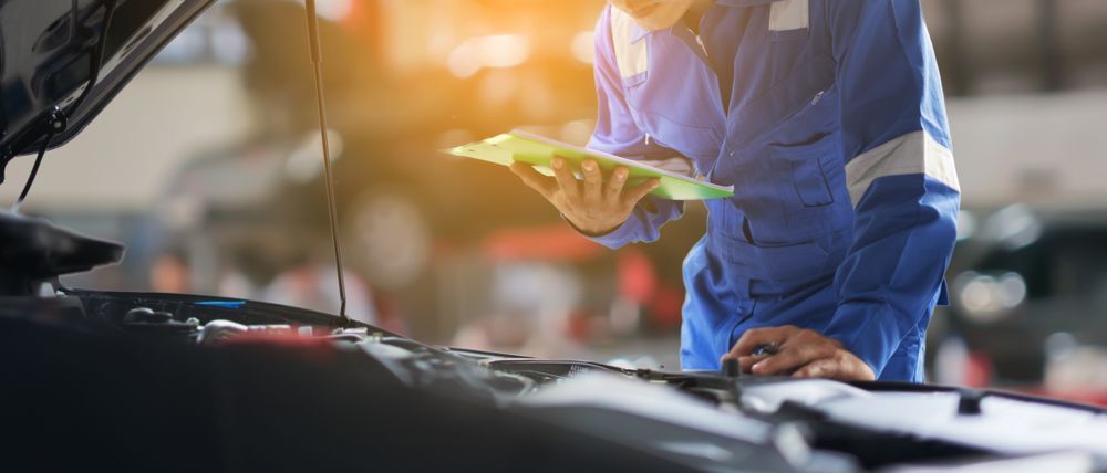A Mechanic is Looking at a Clipboard While Working on a Car — Hive Mobile Roadworthy in Helensvale, QLD