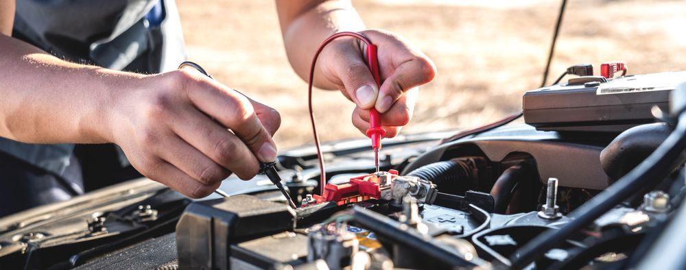 A Man is Working on a Car Battery With a Multimeter — Hive Mobile Roadworthy in Currumbin, QLD