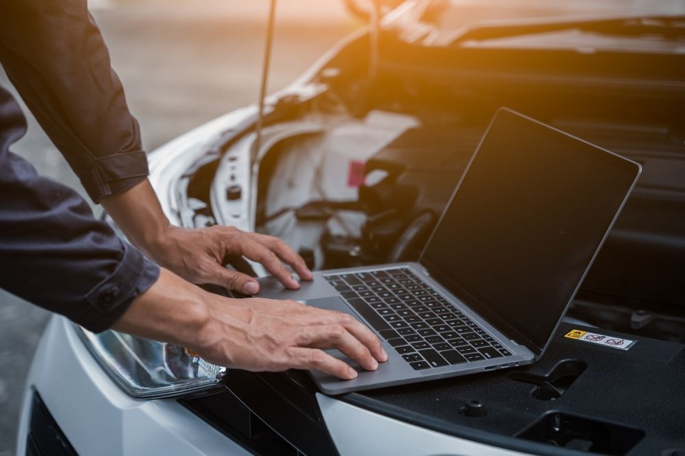 A Man is Using a Laptop Computer Under the Hood of a Car — Hive Mobile Roadworthy in Pimpama, QLD