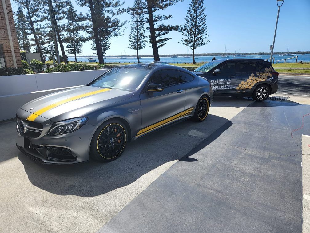 A Grey Car With Yellow Stripes on the Side is Parked Next to a Black Car — Hive Mobile Roadworthy in Helensvale, QLD