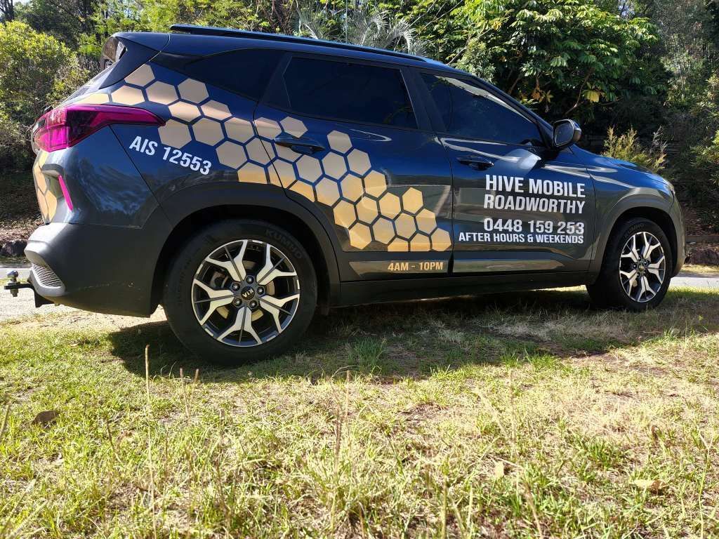 A Car With a Honeycomb Design on the Side is Parked in a Grass Field — Hive Mobile Roadworthy in Robina, QLD