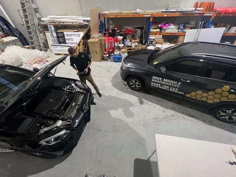 A Man is Standing Next to a Car With the Hood Up in a Garage — Hive Mobile Roadworthy in Robina, QLD