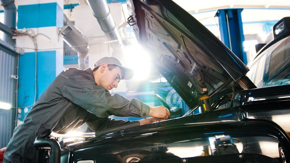 A Man is Working on a Car in a Garage With the Hood Open — Hive Mobile Roadworthy in Mount Nathan, QLD