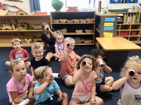 A group of children are sitting on the floor looking through tubes