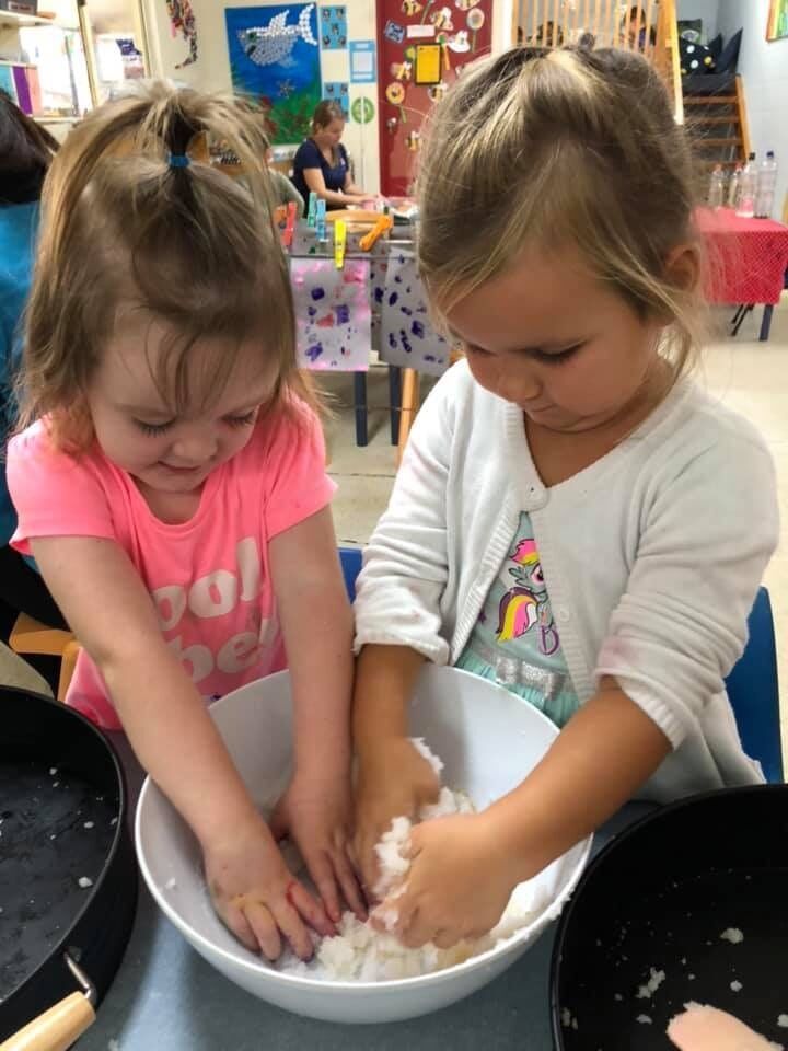 Two little girls are playing with a bowl of food.