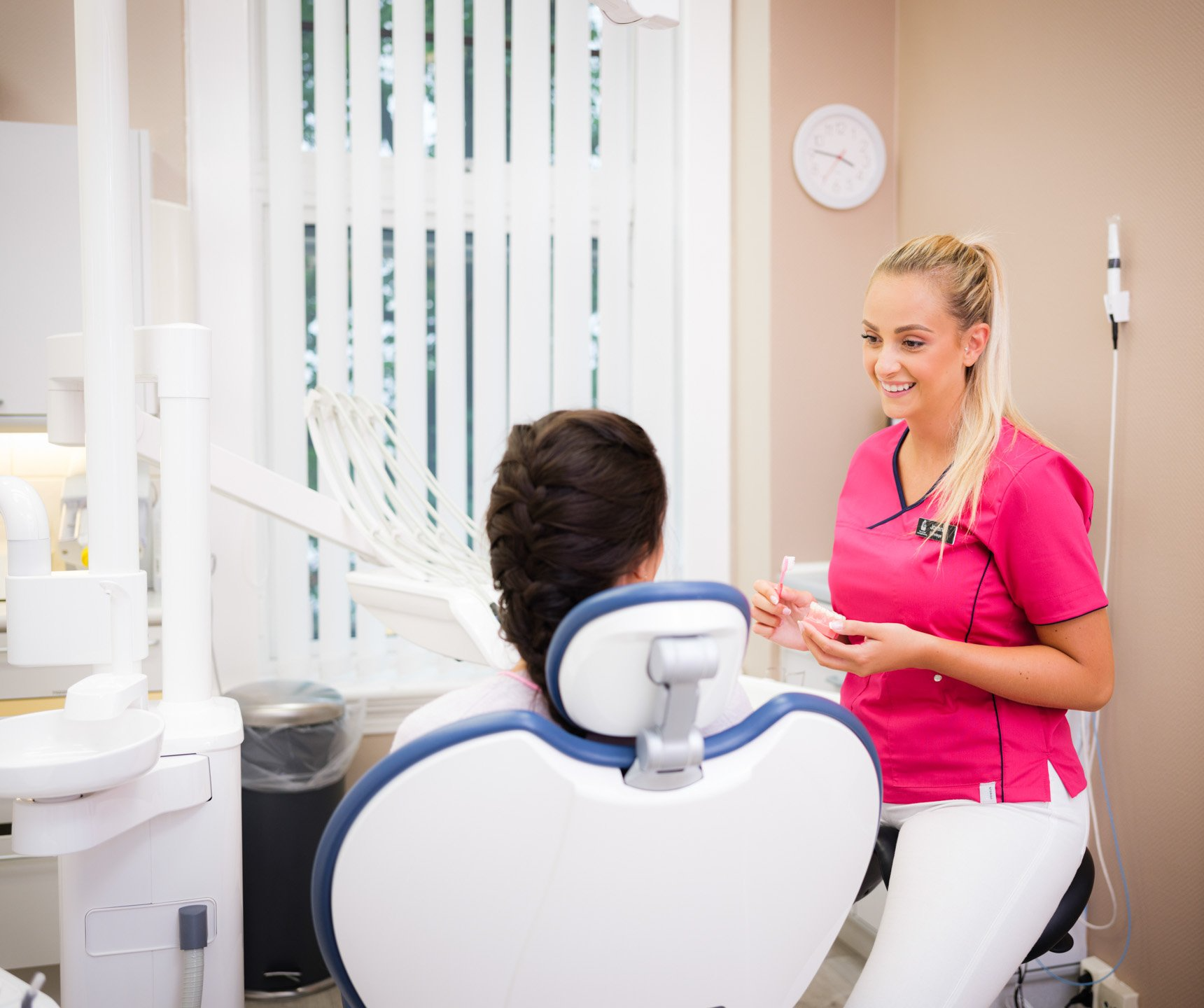 en kvinnelig tannlege snakker med en pasient i en tannlegestol.