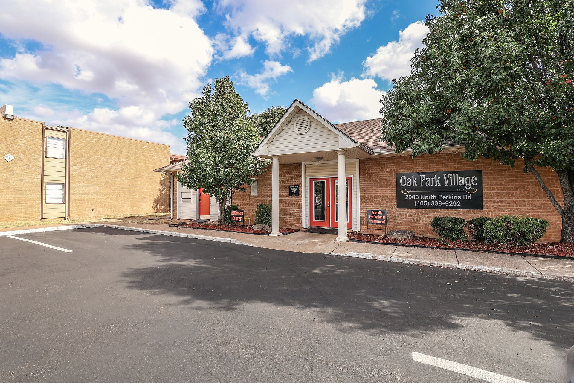 Brick building with red door, white columns, and two trees in front, blue sky in the background.