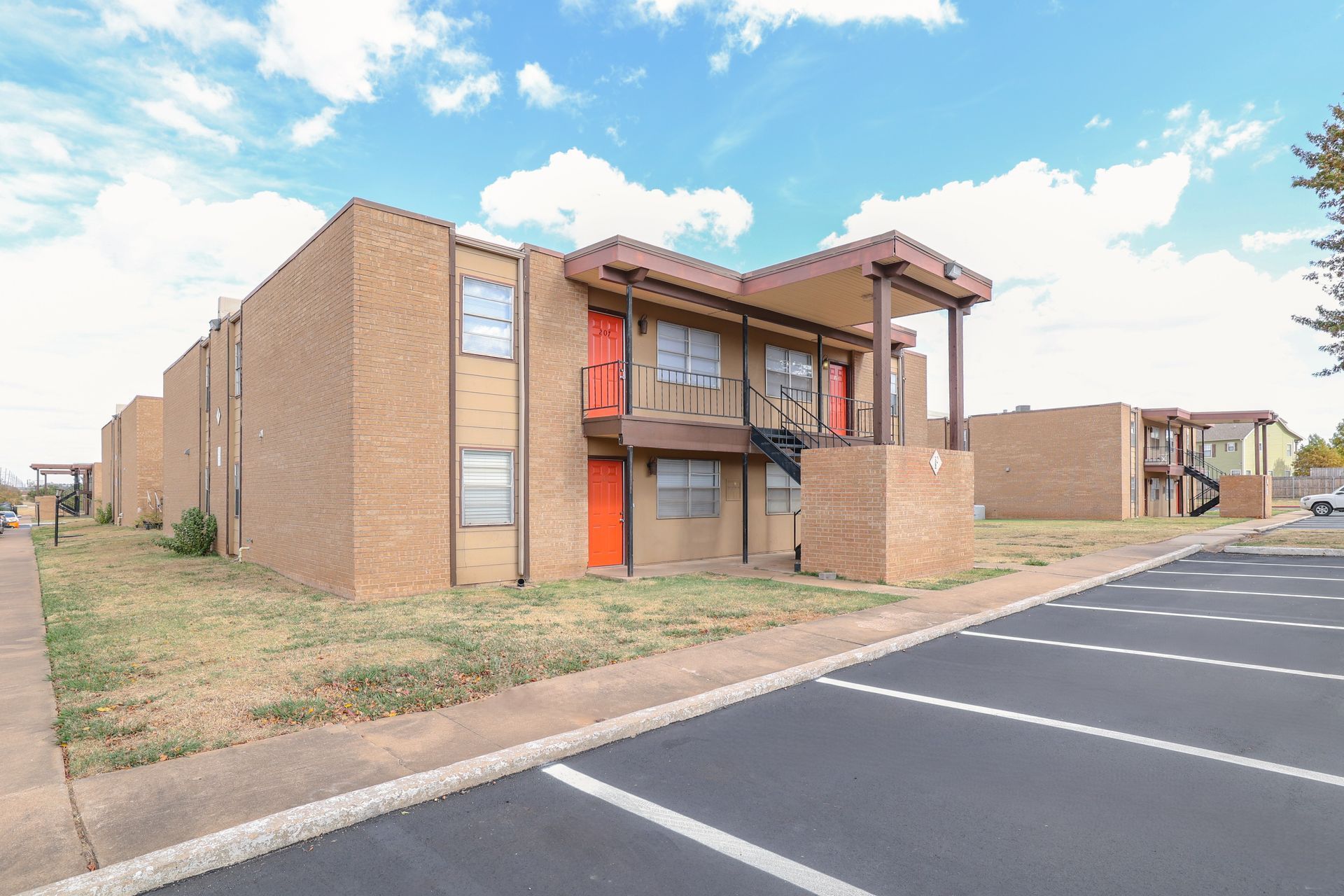 Two-story brick apartment building with parking in front, set against a cloudy blue sky.