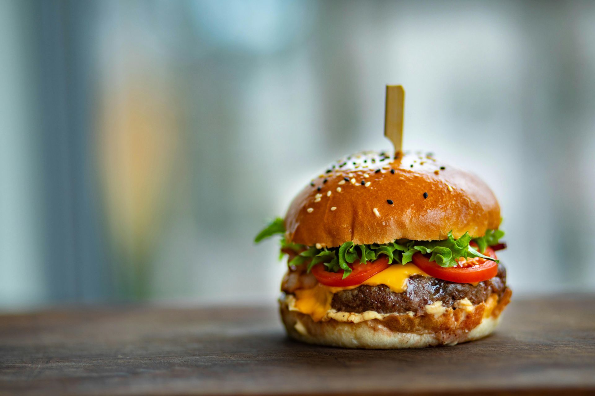 A juicy burger with lettuce, tomato, and melted cheese on a sesame bun is skewered on a wooden board.