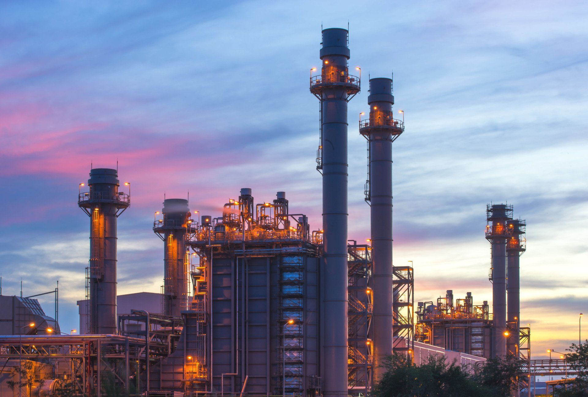 Eine große Industrieanlage mit vielen Schornsteinen bei Sonnenuntergang.