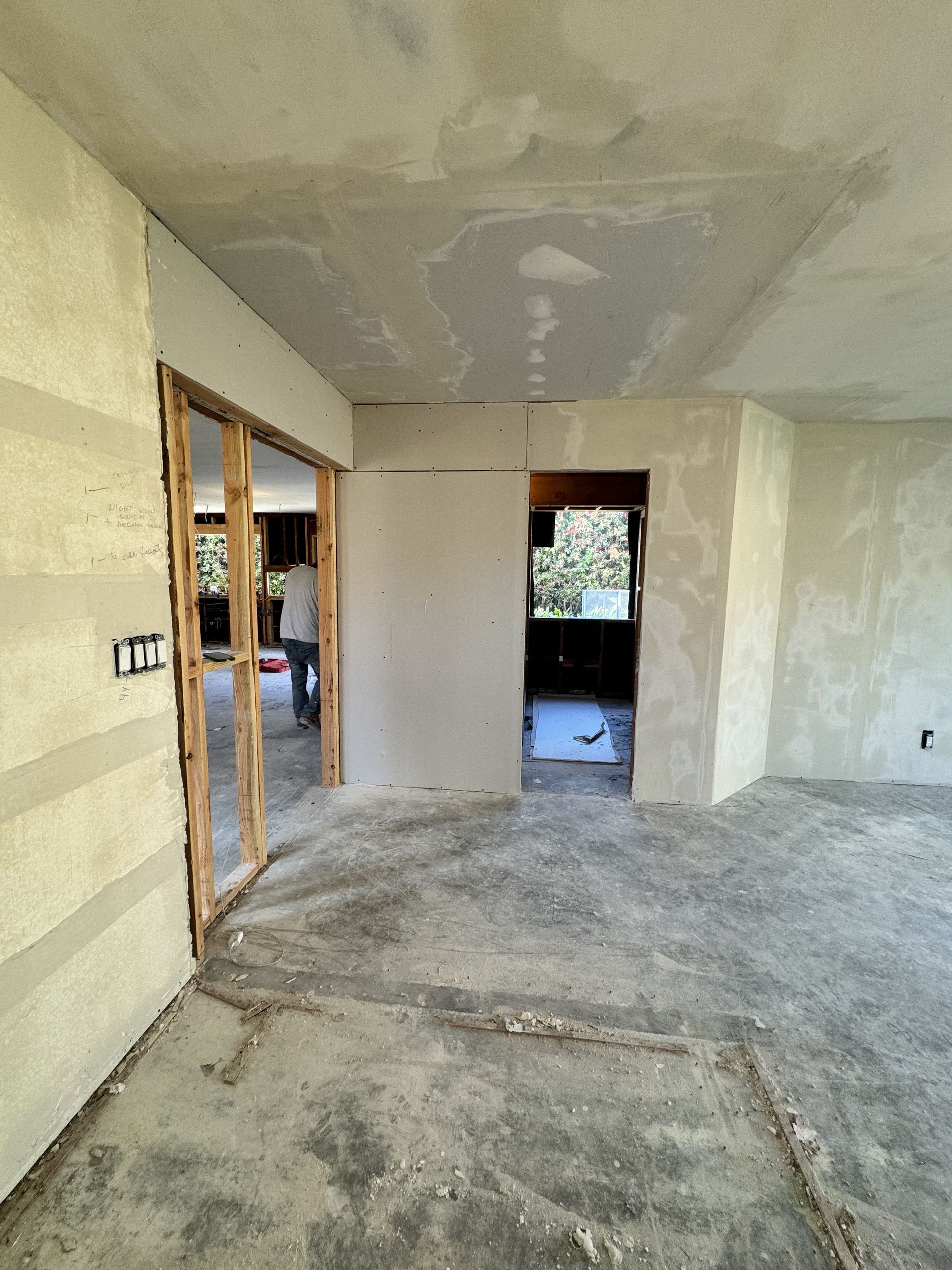 Unfinished room with plastered walls, concrete floor, and open doorway to another room.