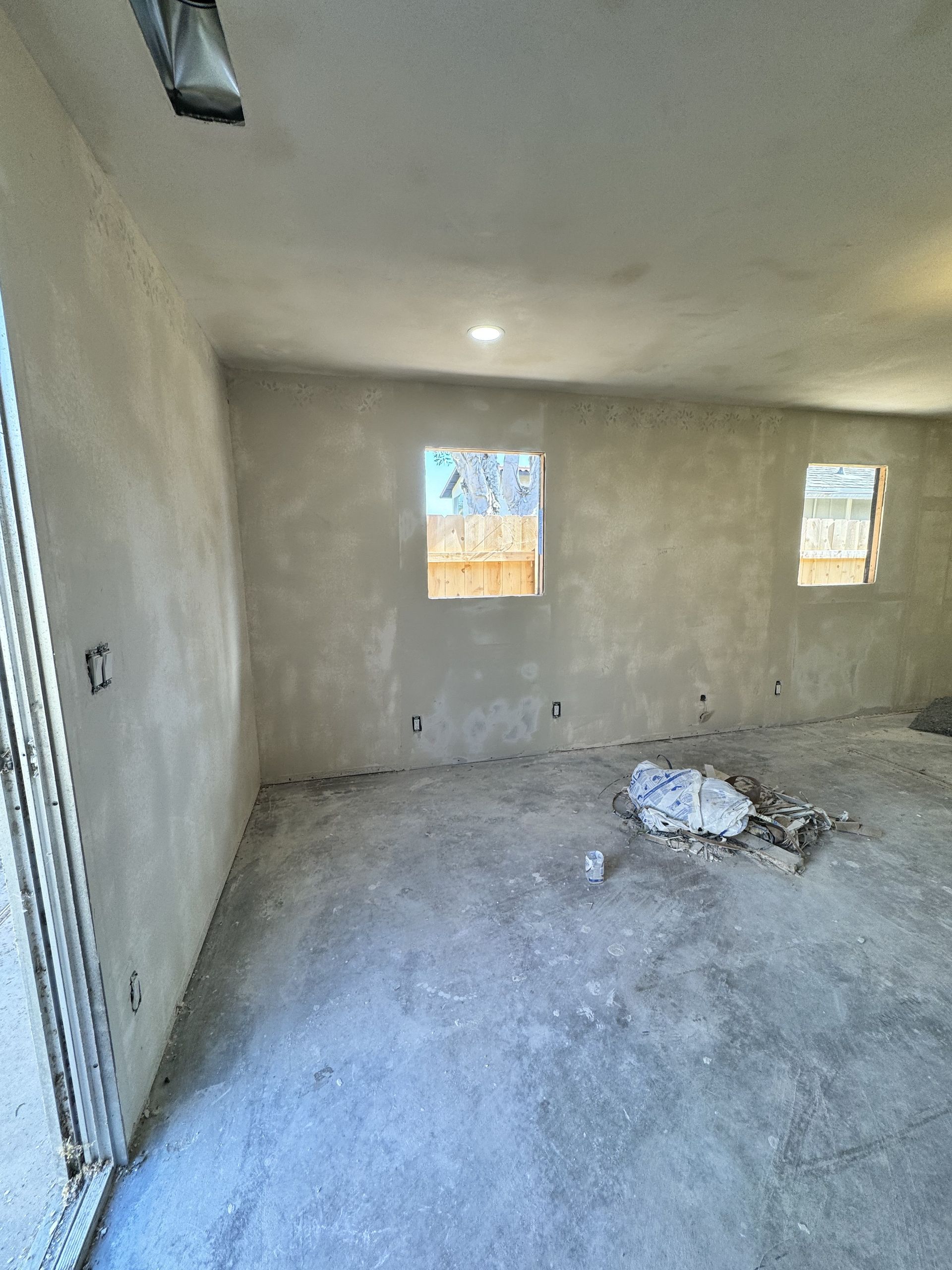 Empty unfinished room with bare plaster walls, concrete floor, and two small windows.