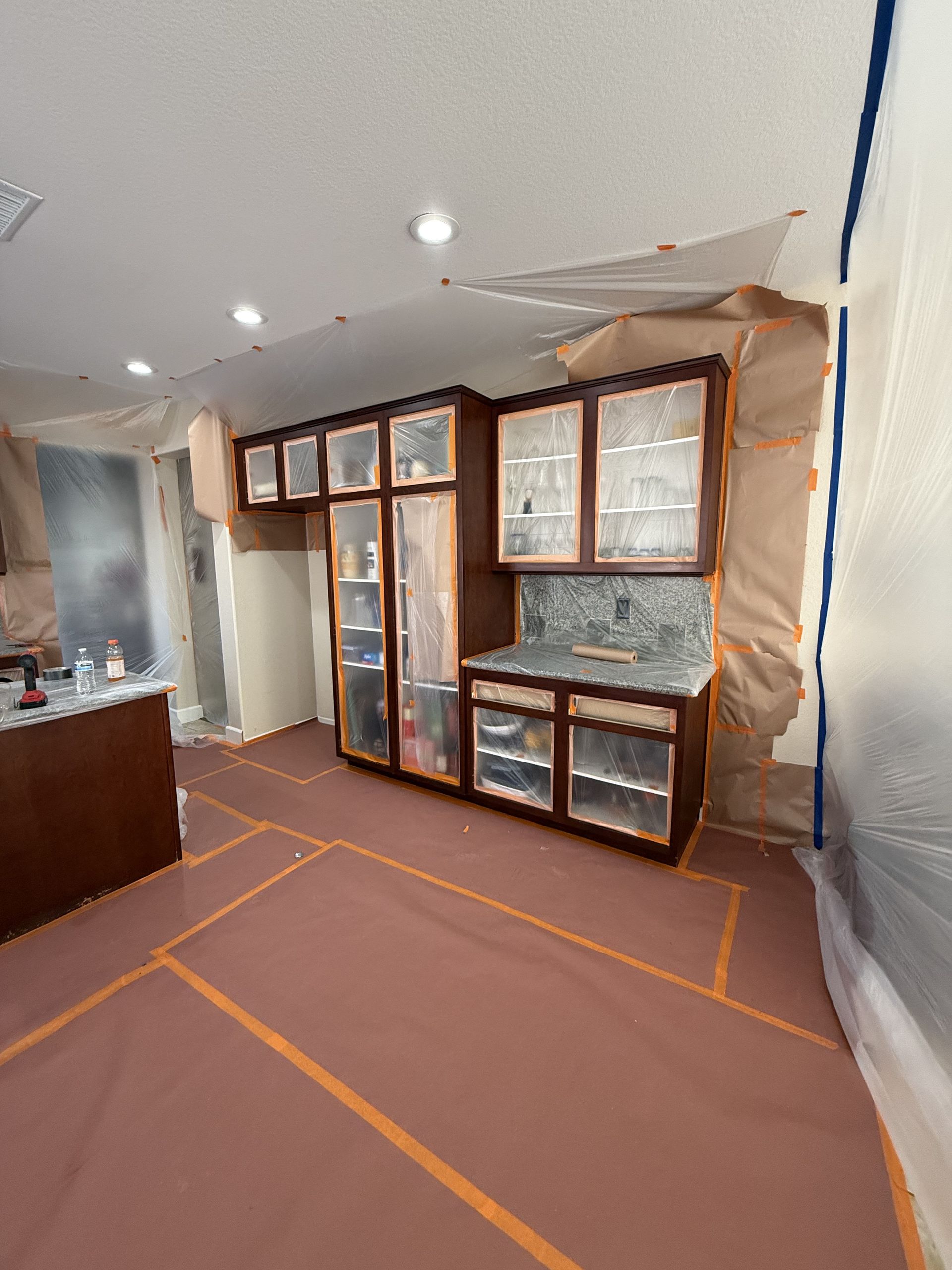 Renovated kitchen with wood cabinets, windowed back wall, and protective plastic sheeting on the floor and right wall