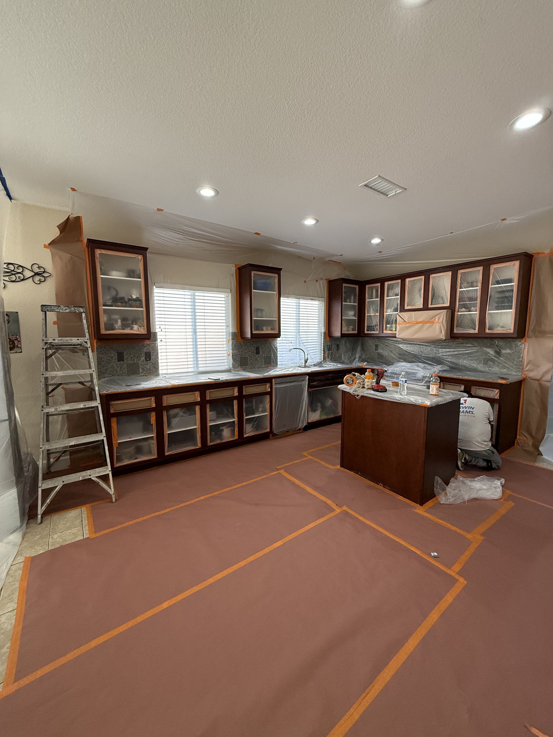 Kitchen under renovation with cabinets, ladder, and taped-off floor area