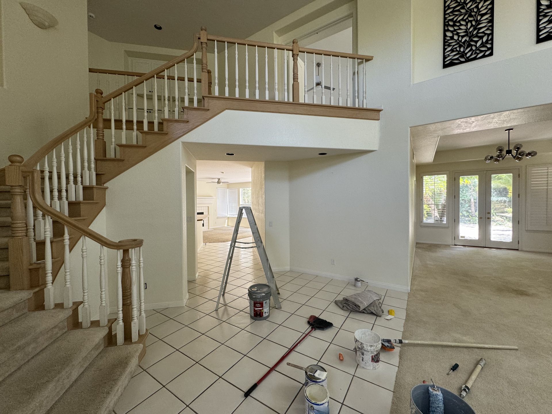 Empty living room with stairs, tiled floor, and a ladder amid renovation clutter