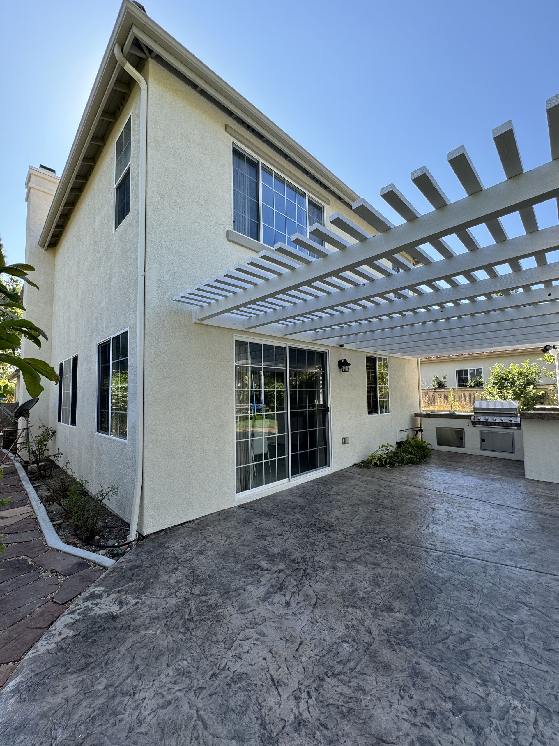 Modern two-story house exterior with white stucco, large windows, and a pergola-covered driveway
