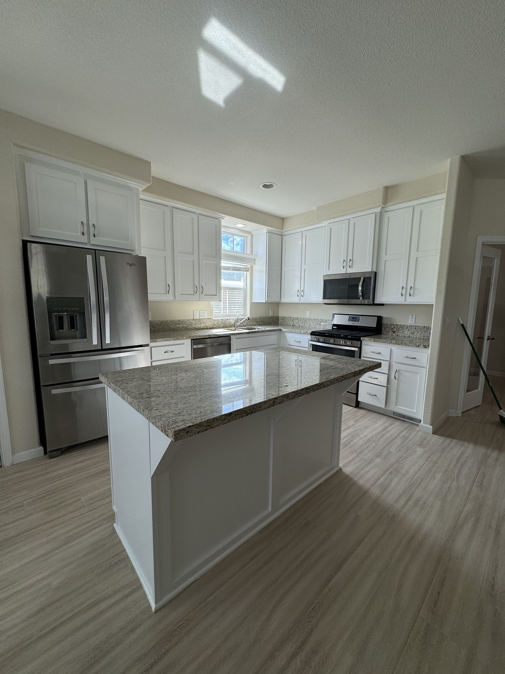 Bright modern kitchen with white cabinets, stainless steel appliances, and a large granite island