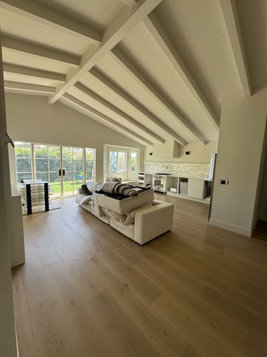 Bright open living room with vaulted ceiling, white sofa, wood floors, and large windows overlooking greenery