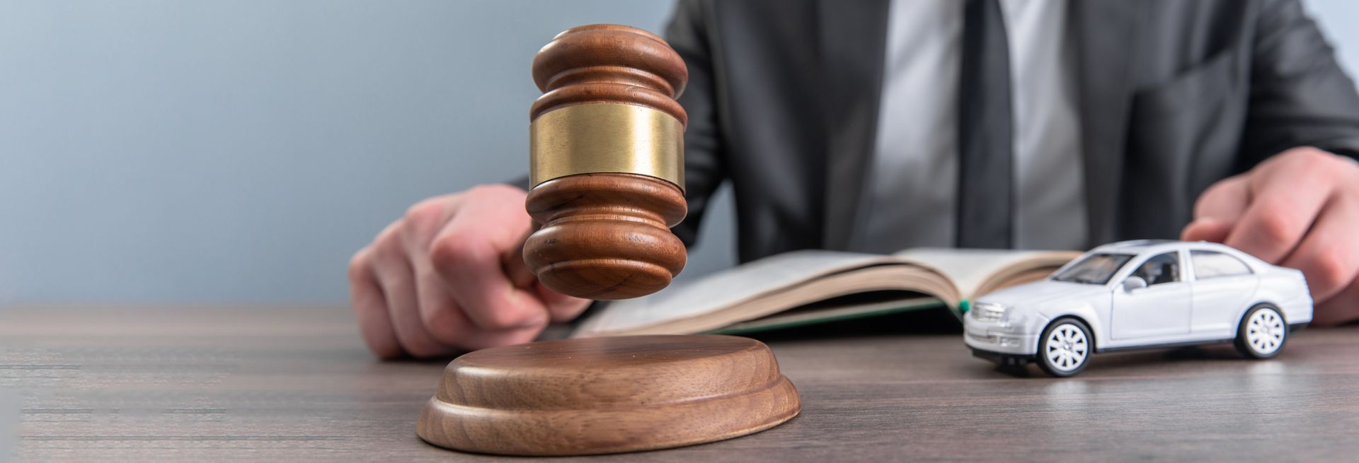 Auto accident lawyer holding a wooden gavel, with a toy car and a book on the table.