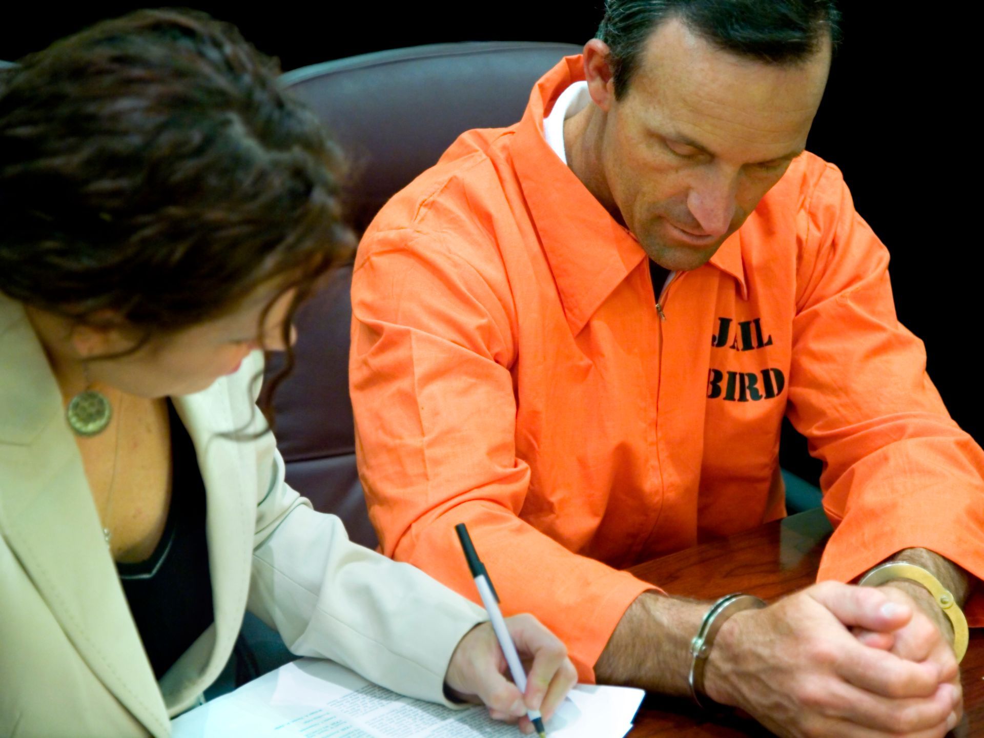 A female defense attorney sits next to her client, while writing on a document.