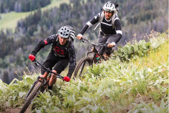 Two people are riding bicycles down a grassy hill.