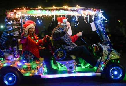 A group of people are riding in a golf cart decorated with christmas lights.