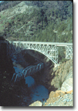 A bridge over a river surrounded by mountains and trees.