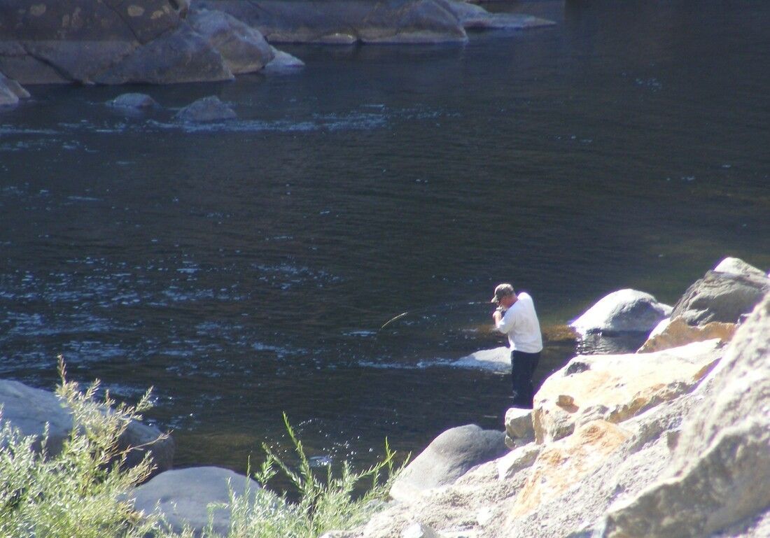 A man is fishing in a river while standing on a rock.