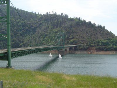 Two sailboats are going under a bridge over a lake.
