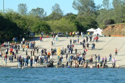 A large group of people are gathered on the shore of a lake