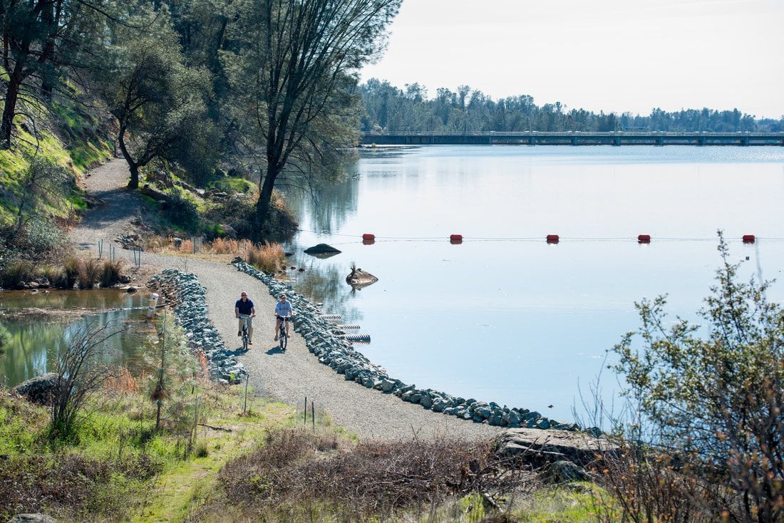 A couple of people are walking along a path next to a lake.