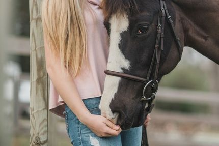 A woman is holding a black and white horse in her arms.