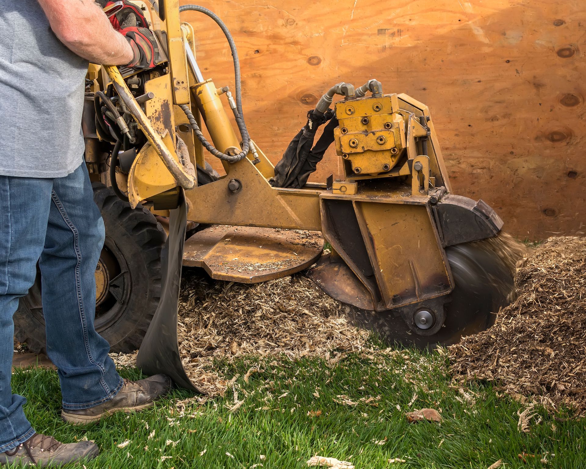 Yellow excavator digging dirt beside a wooden wall while a worker stands nearby. Yellow excavator digging dirt beside a wooden wall while a worker stands nearby.
