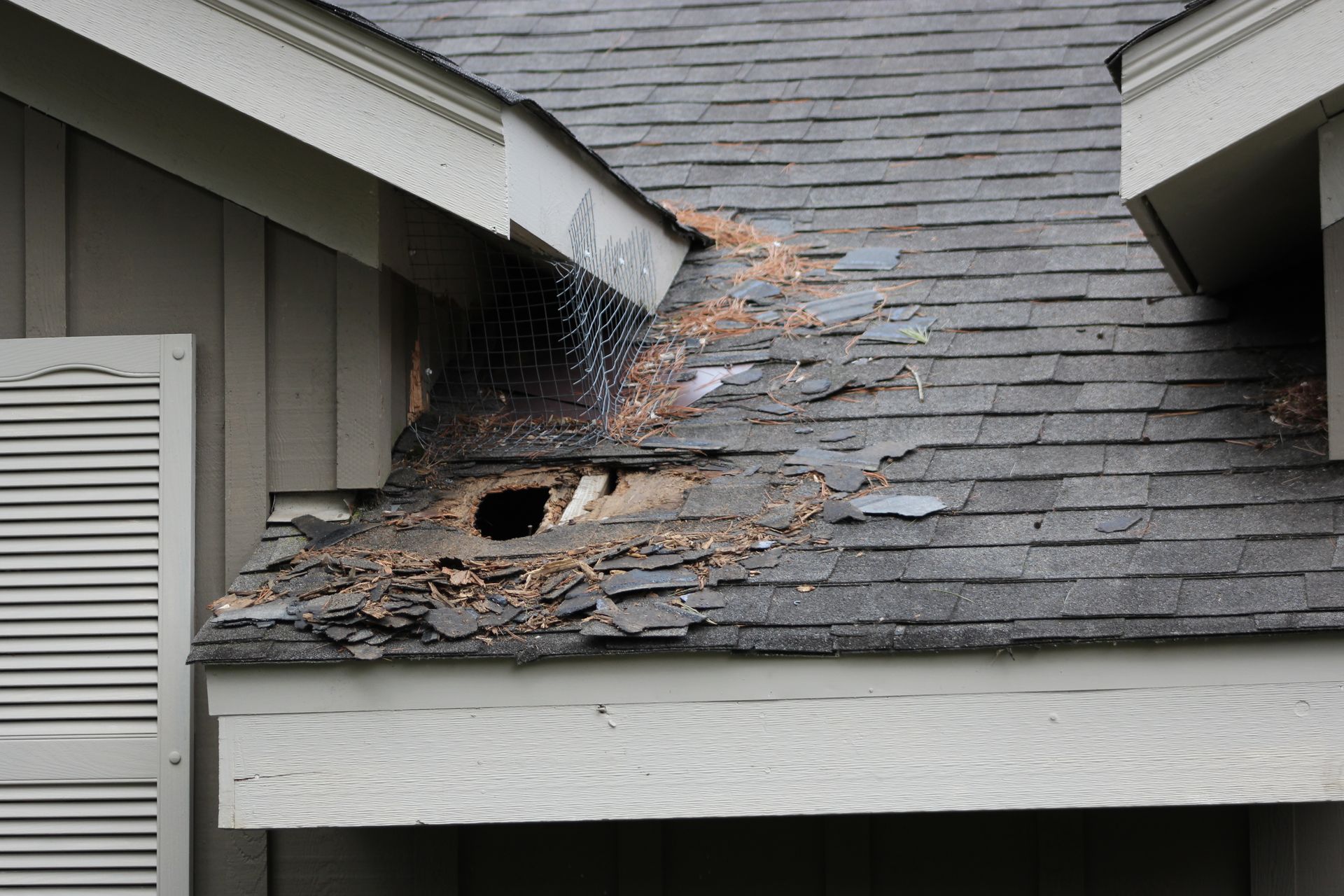 Damaged asphalt shingle roof with a large hole, exposing the underlying structure.
