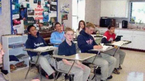 Students sit at desks in a classroom, listening to a lecture with a wall display about the ocean in the background.