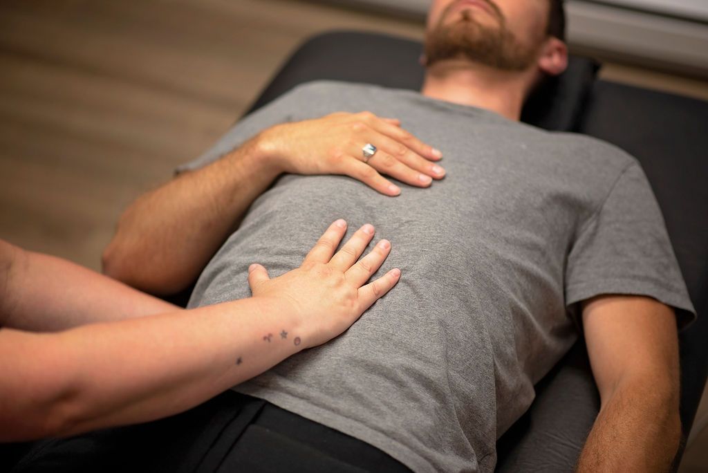 Person receiving abdominal massage, lying on a massage table. Therapist's hands on patient's chest and abdomen.