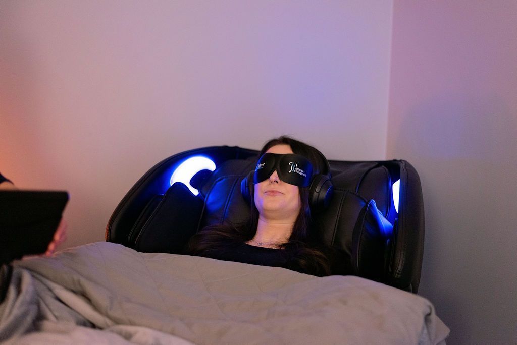 Person wearing eye mask and headphones in a relaxation chair with blue lights; indoors.