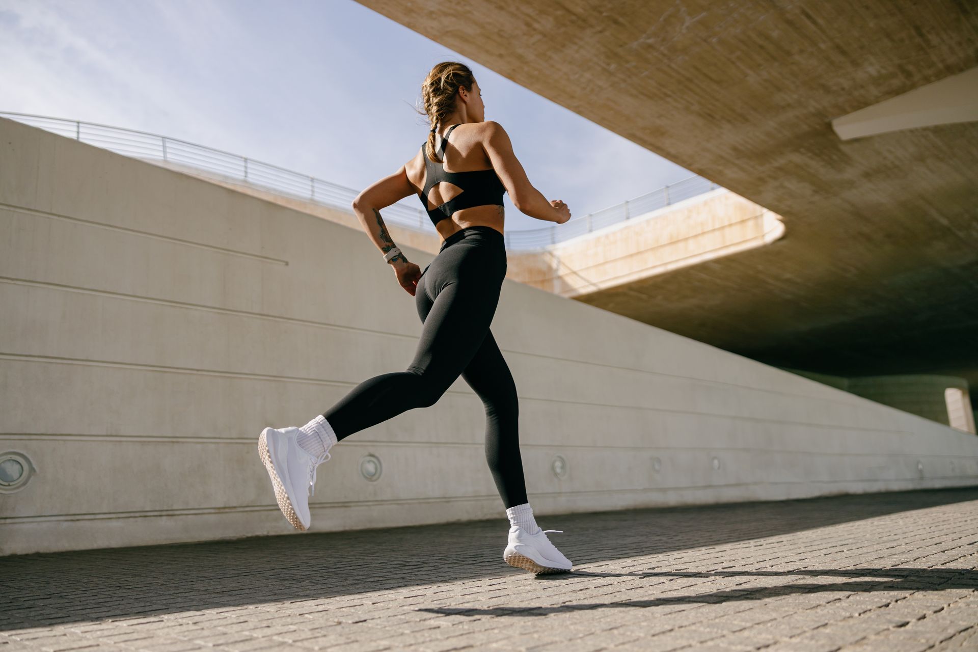 Woman in athletic wear running under a modern concrete structure.