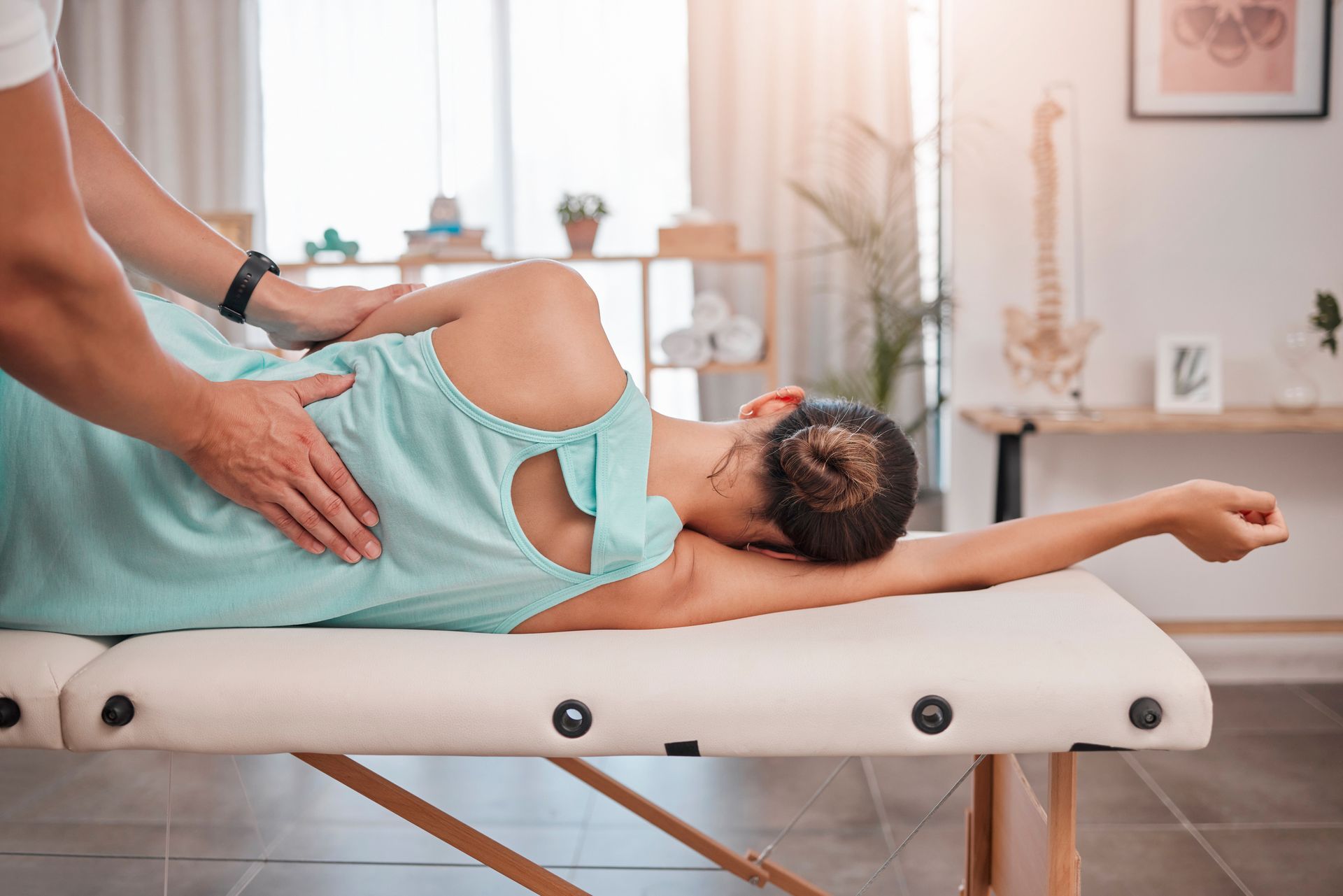 A person in a light blue top receives a spinal adjustment from a practitioner on a treatment table in a clinic.
