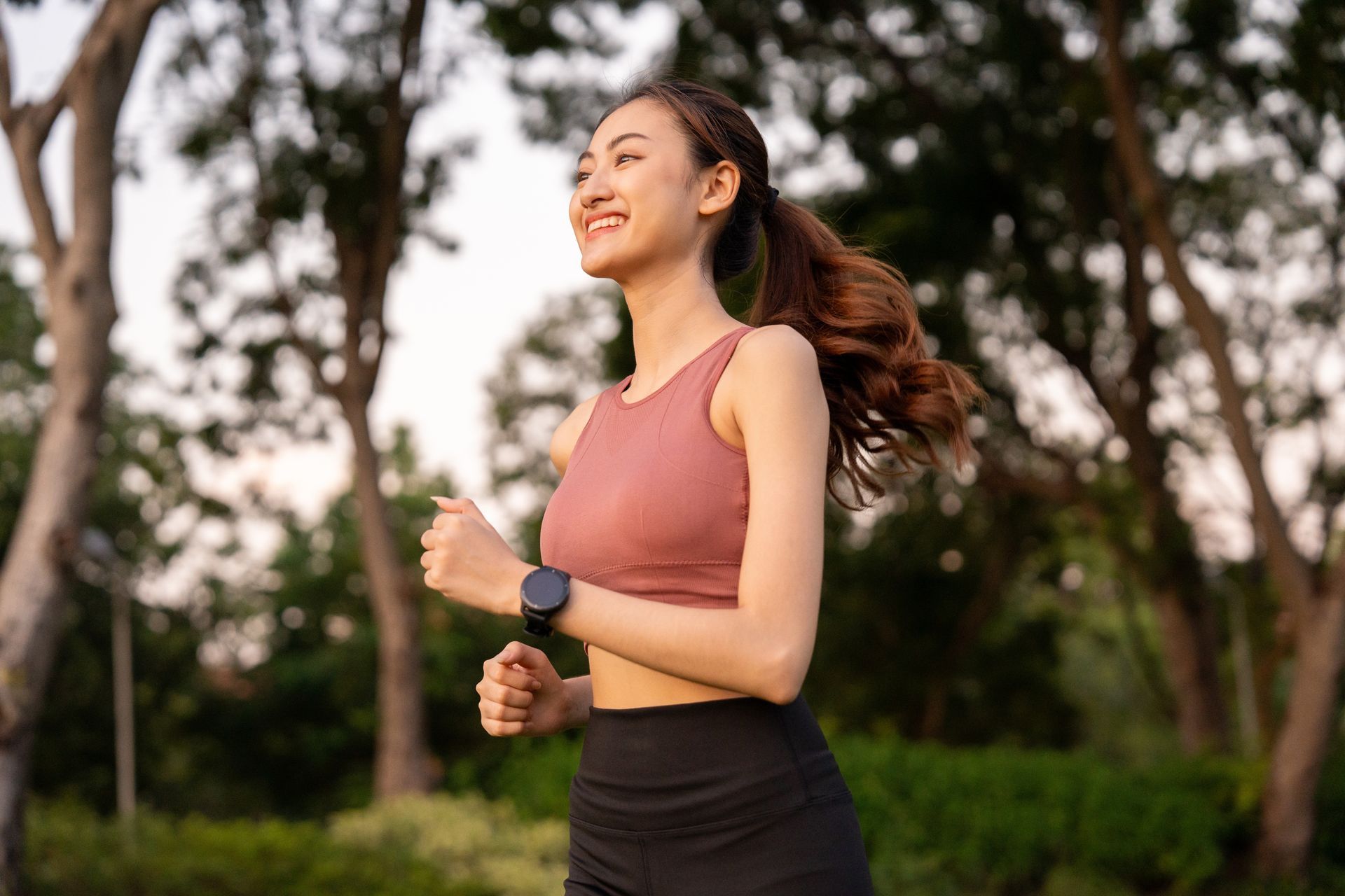 Woman jogging outdoors in a pink top and black leggings at sunset