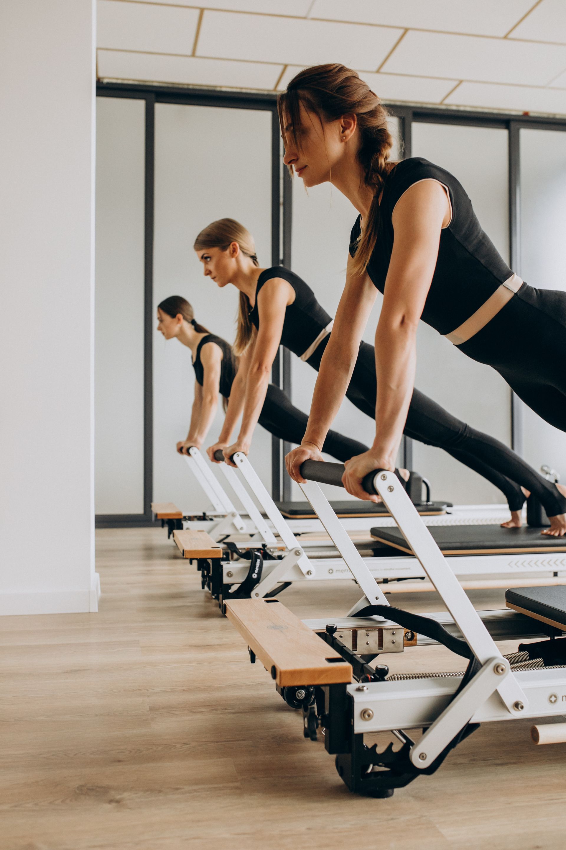 A group of women are doing pilates exercises on pilates machines in a gym.