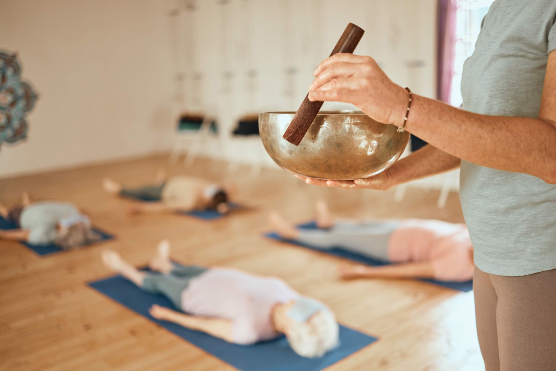 a woman is holding a singing bowl in front of a group of people laying on yoga mats
