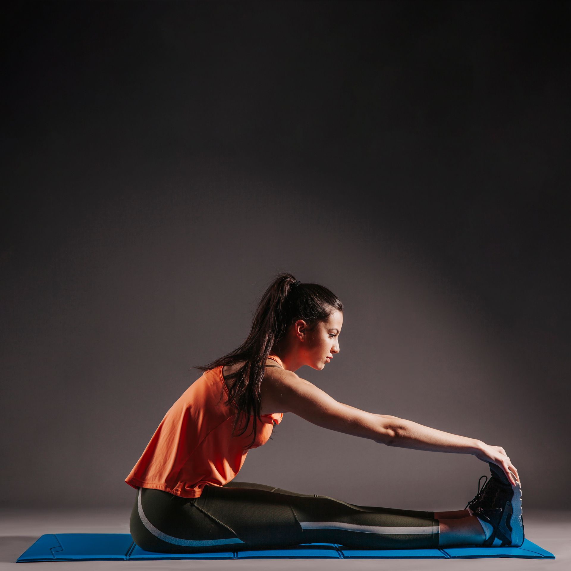A woman is sitting on a yoga mat stretching her legs.