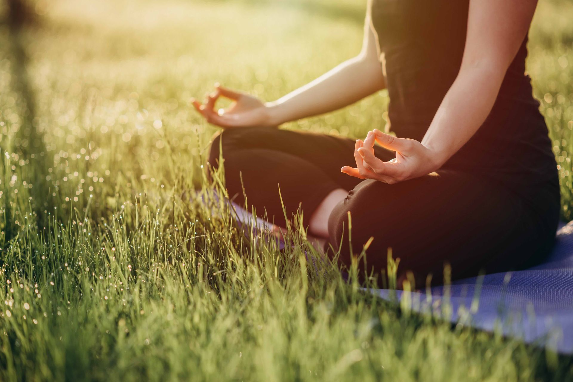 a woman sits in a lotus position on a yoga mat in the grass