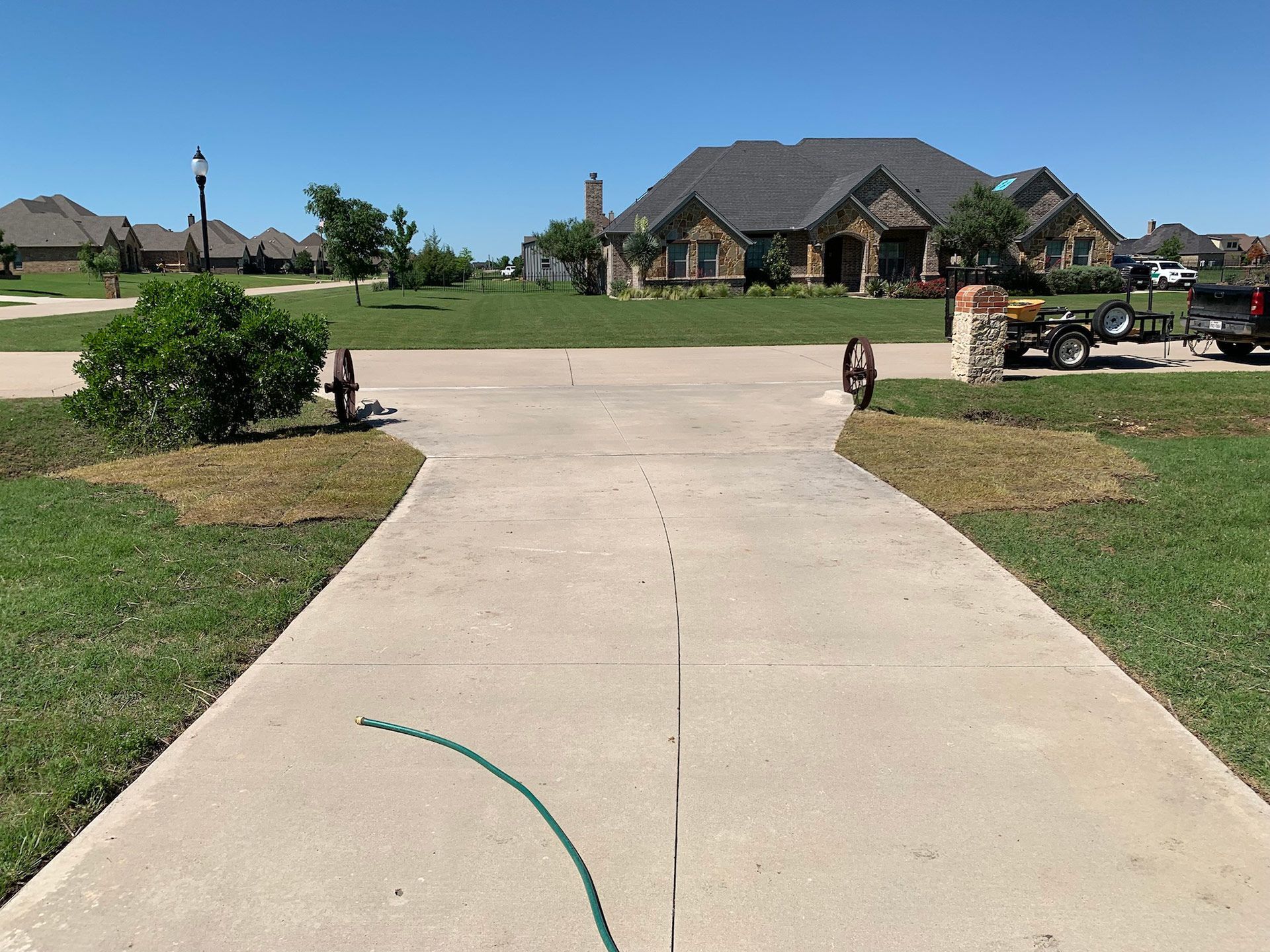 Concrete driveway leading to a large house with a green lawn on a sunny day.