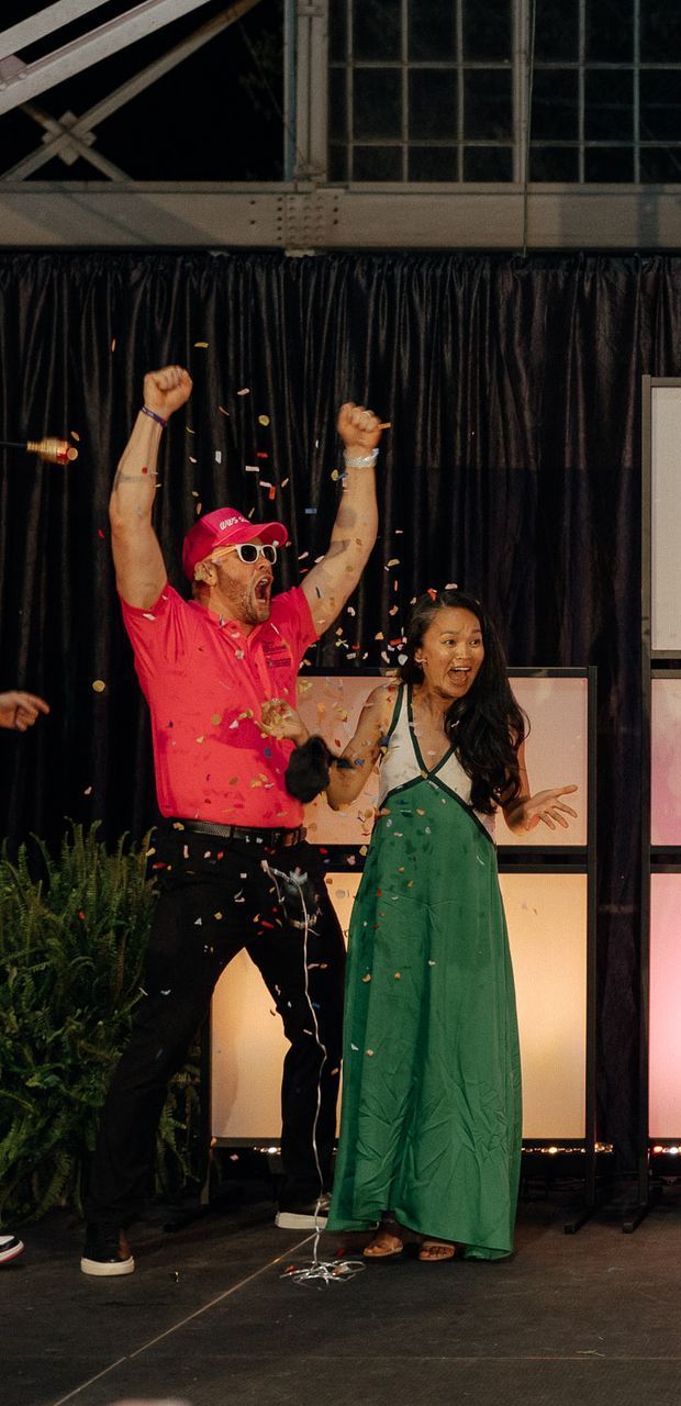 A man in a pink shirt and a woman in a green dress are dancing on a stage.