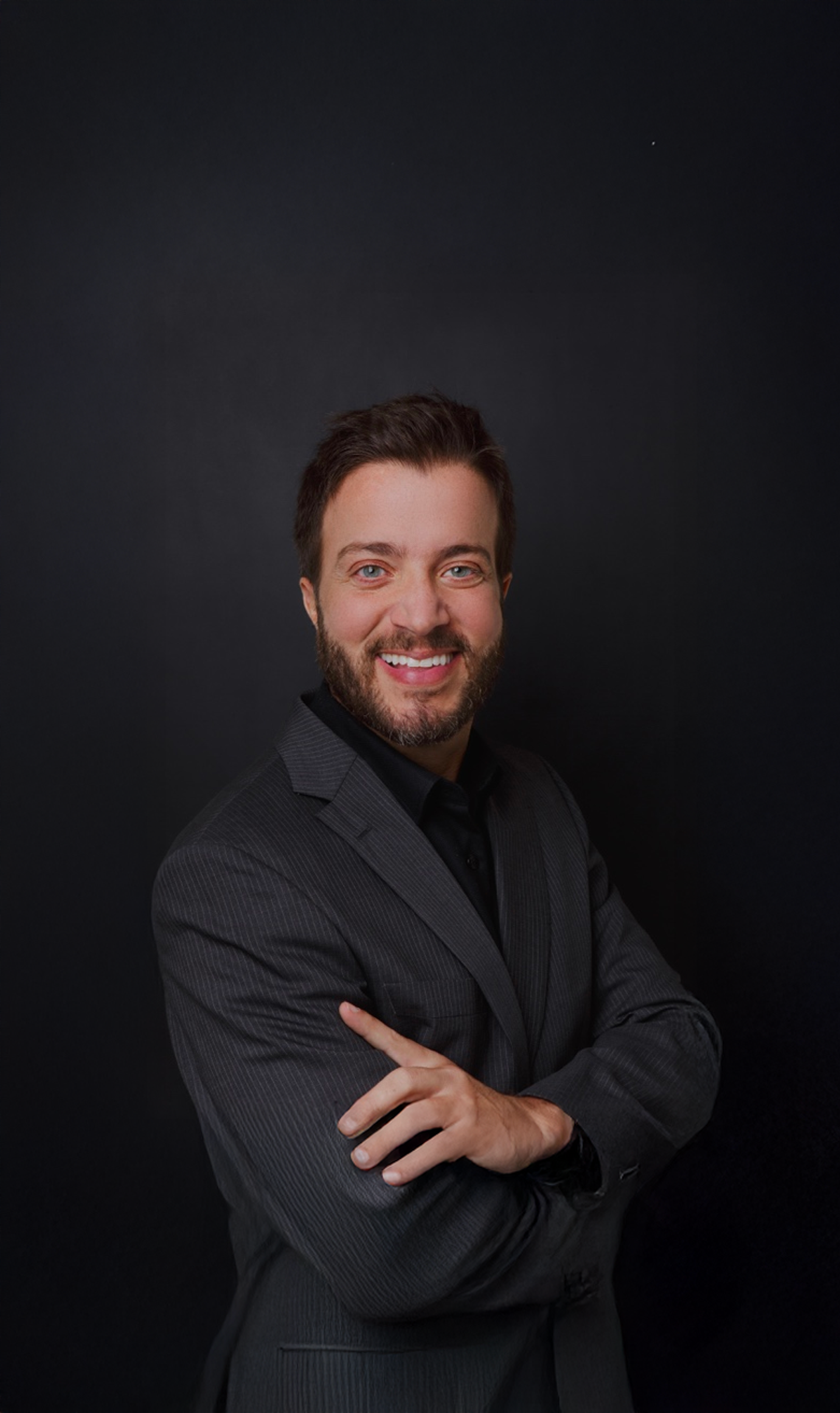 Homem de jaleco branco, camisa escura e barba, olhando para a câmera.