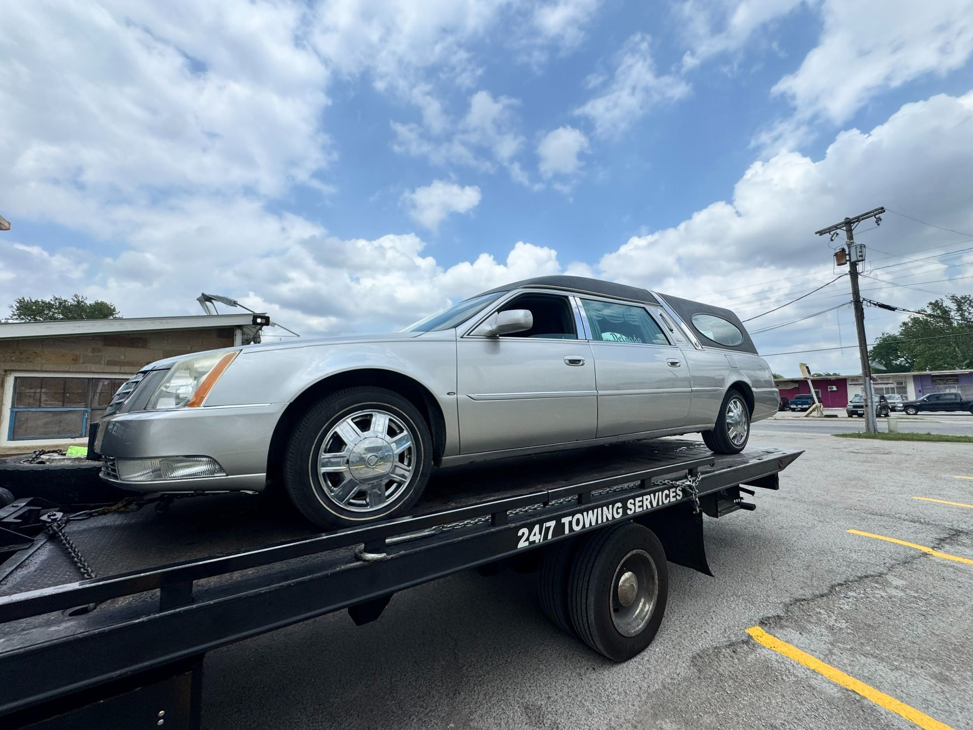 A yellow tow truck is hitched to and towing a silver SUV along a highway on a sunny day.