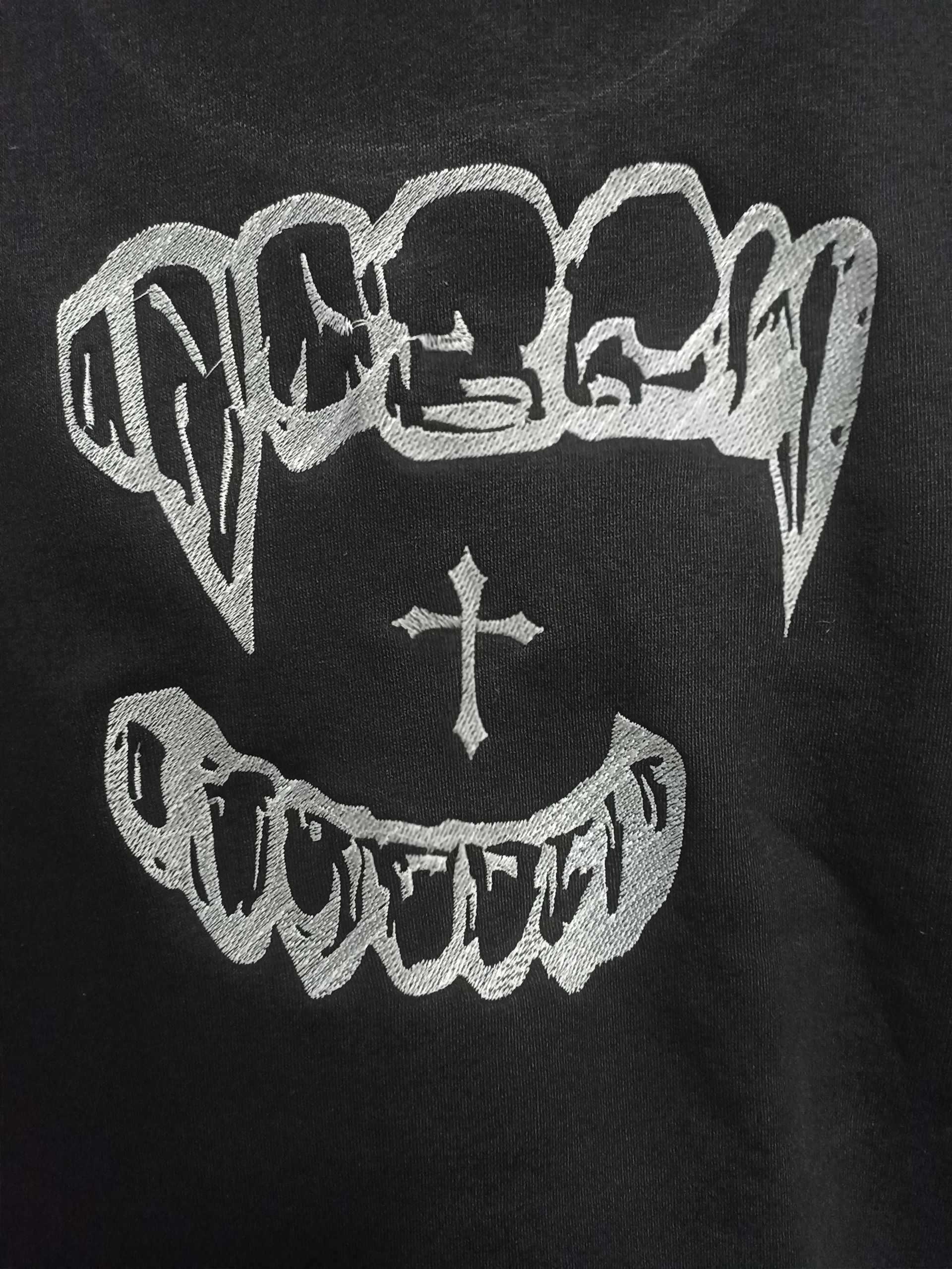 Una maglietta nera ha un disegno di denti da vampiro e una croce sopra